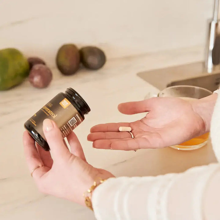 Hand holding Liposomal Resveratrol Purovitalis bottle pouring capsules to the other hand.
