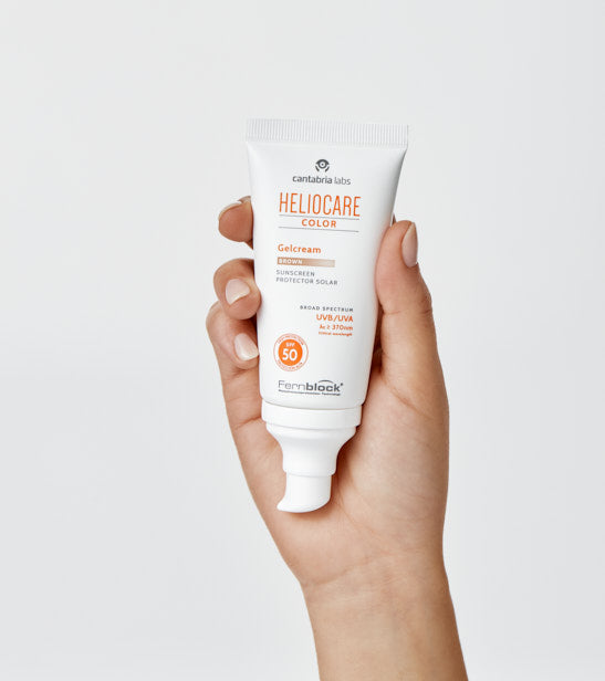 Hand holding a tube of Heliocare Color Gelcream on a light gray background