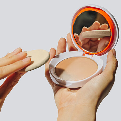 Compact powder with a mirror and a sponge held by hands against a light background