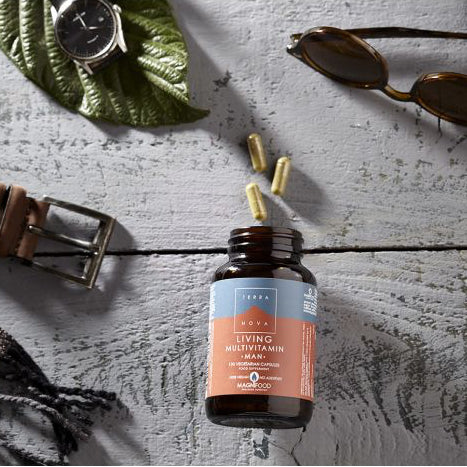 Bottle of living well man supplement on a wooden surface with sunglasses, belt, and leaf.
